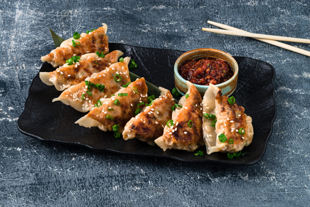 Traditional asian pan fried gyoza dumplings with a dip sauce, japaneese gyoza dumplings with meat and mushrooms on ceramic plate